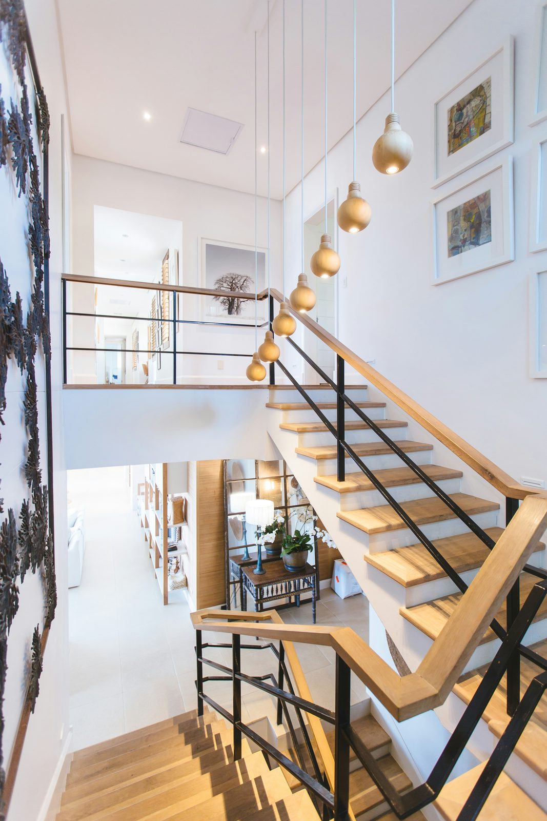 Open timber and steel staircase lit by a cascade of pendant bulbs beside a framed gallery wall
