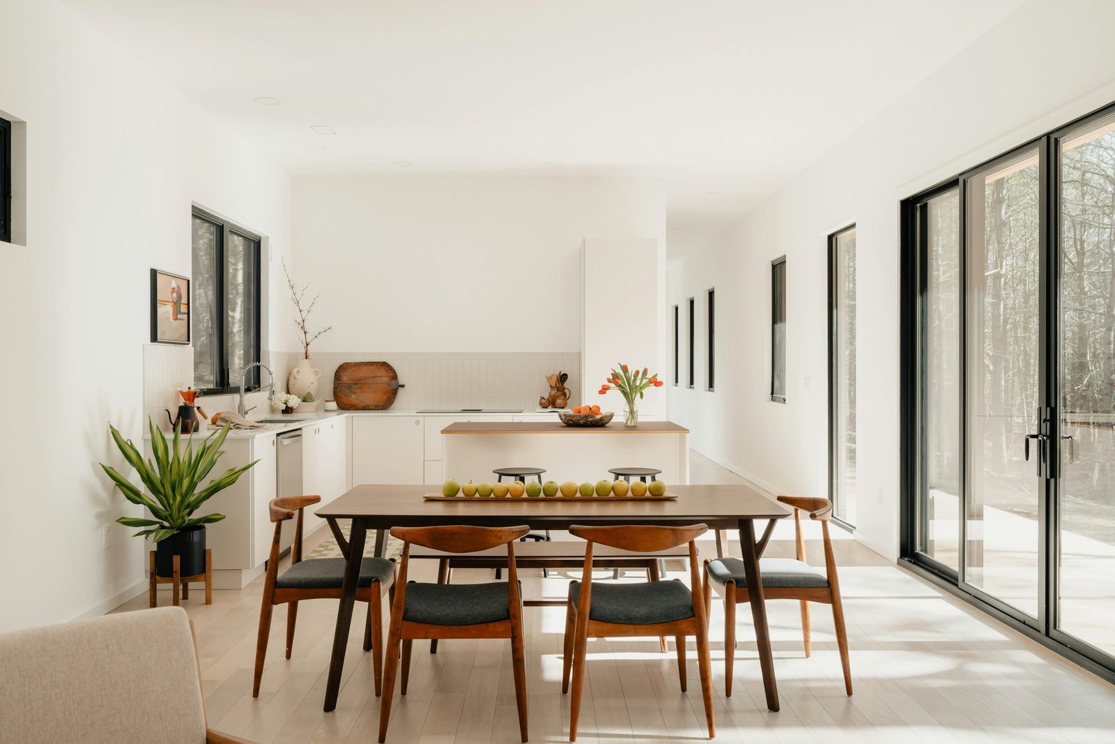 Bright minimalist kitchen and dining area with mid-century walnut chairs and large sliding glass doors
